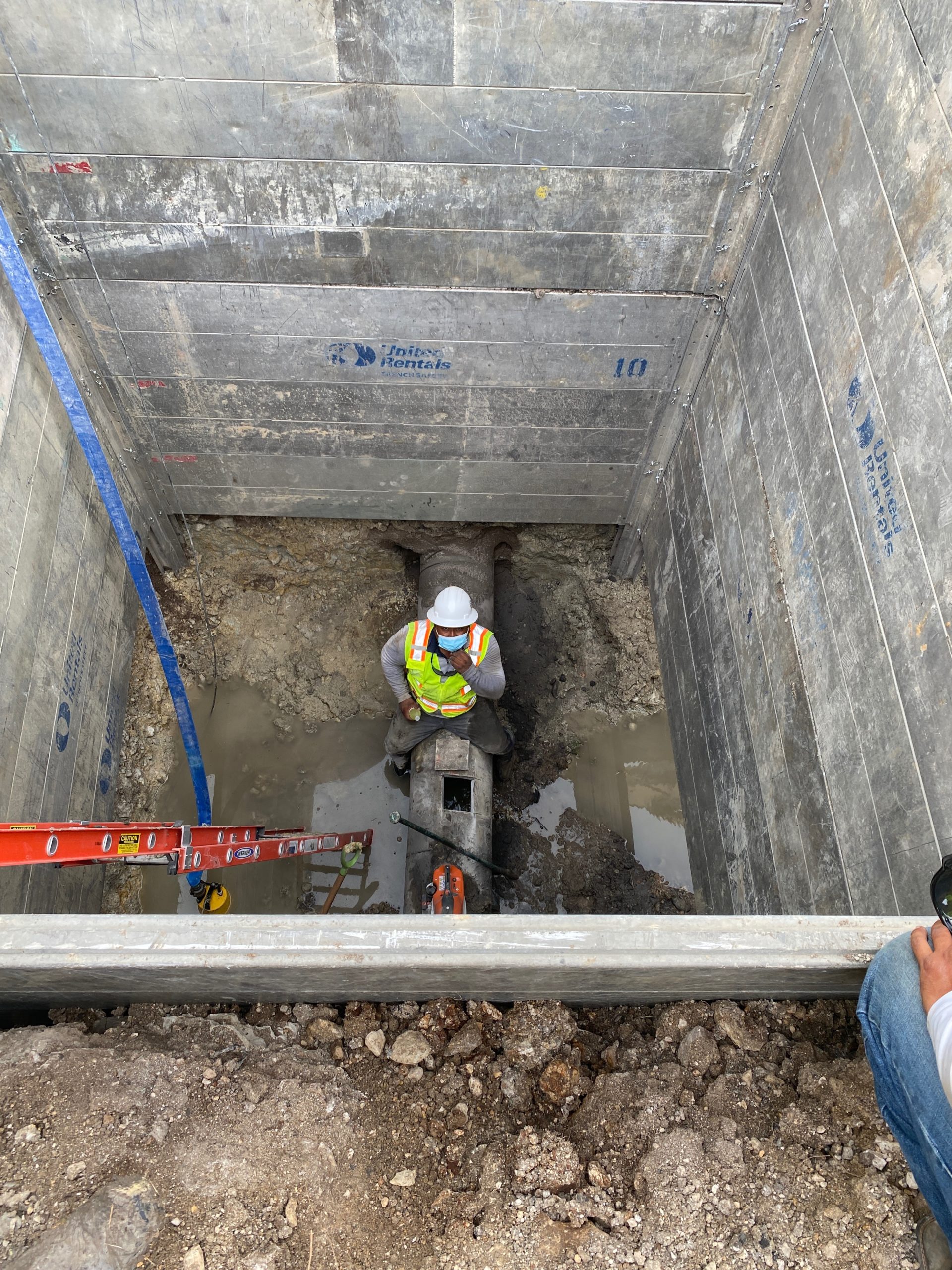 Worker sitting on to of pipe inside of a big concrete hole.